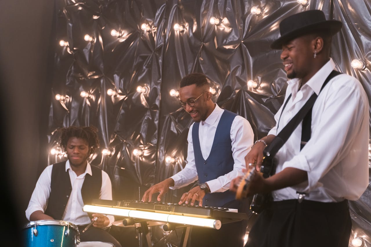 Vibrant scene of three musicians performing with drums, keyboard, and guitar on a lit stage.
